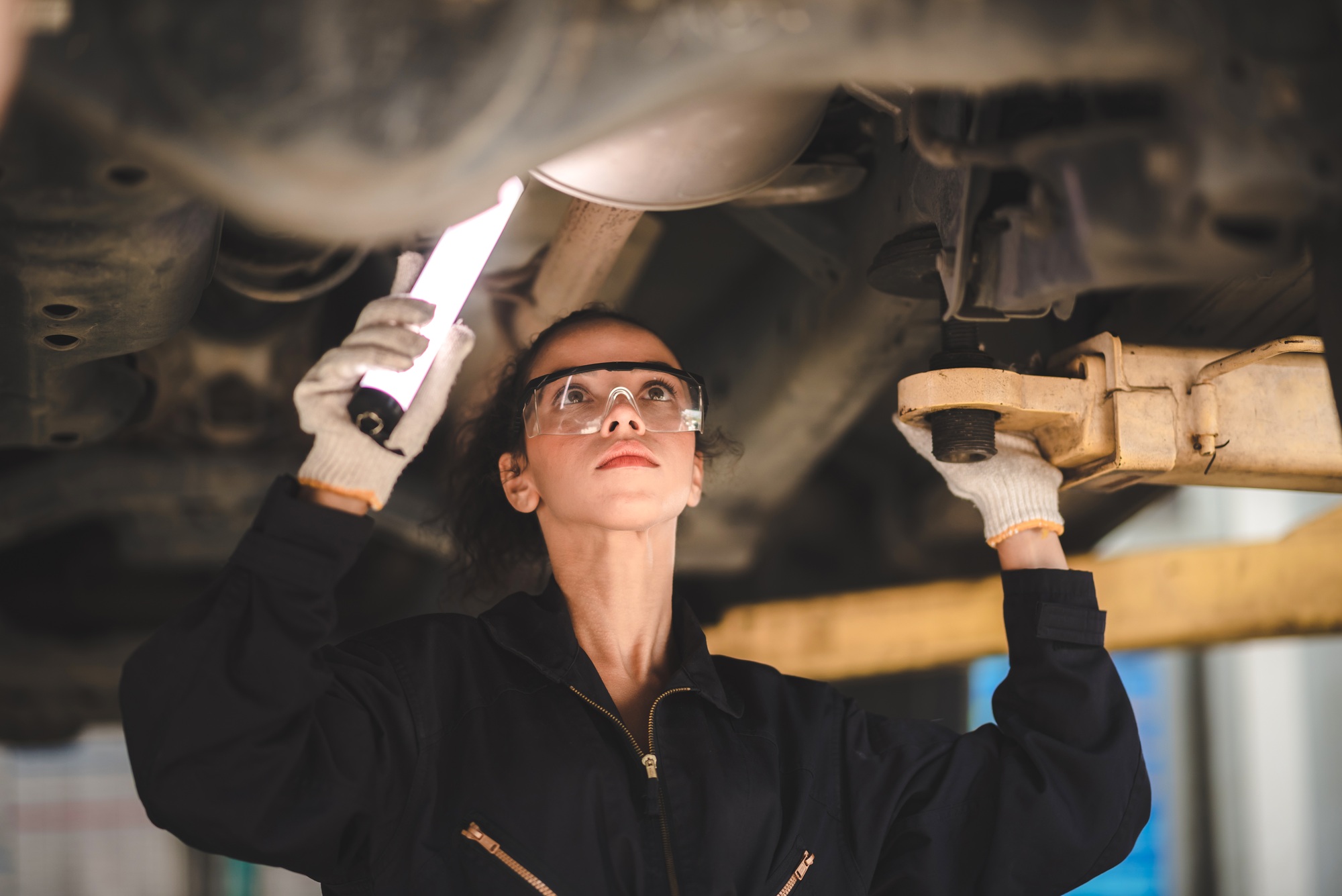 car mechanic standing under car in garage inspecting and doing maintenance work for car