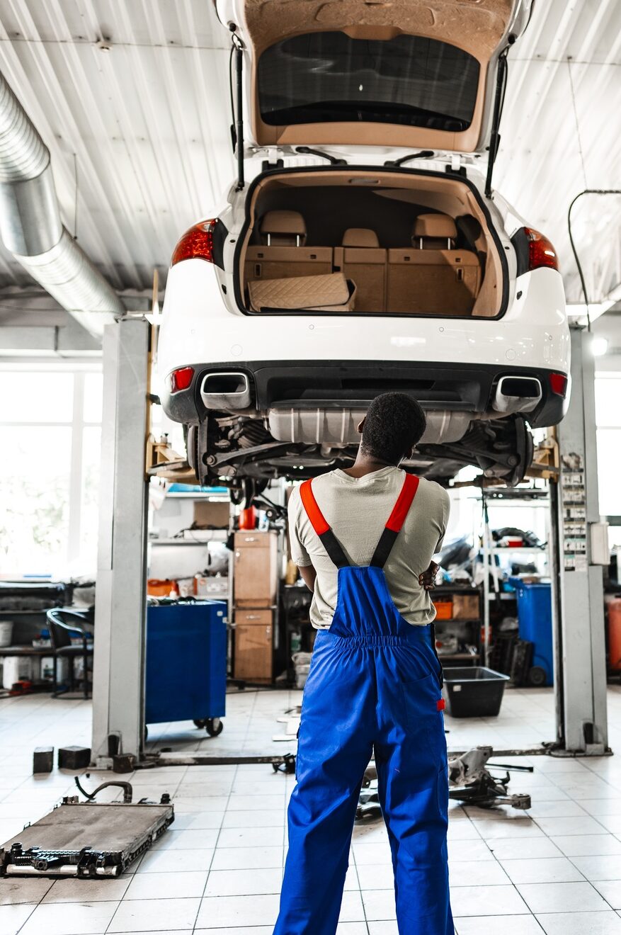 Pensive young African mechanic in car service looking at car thinking of how to repair it